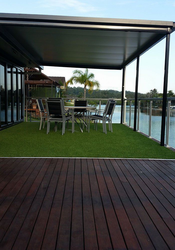 Covered patio with dining table, green turf, and waterfront view beside a wooden deck