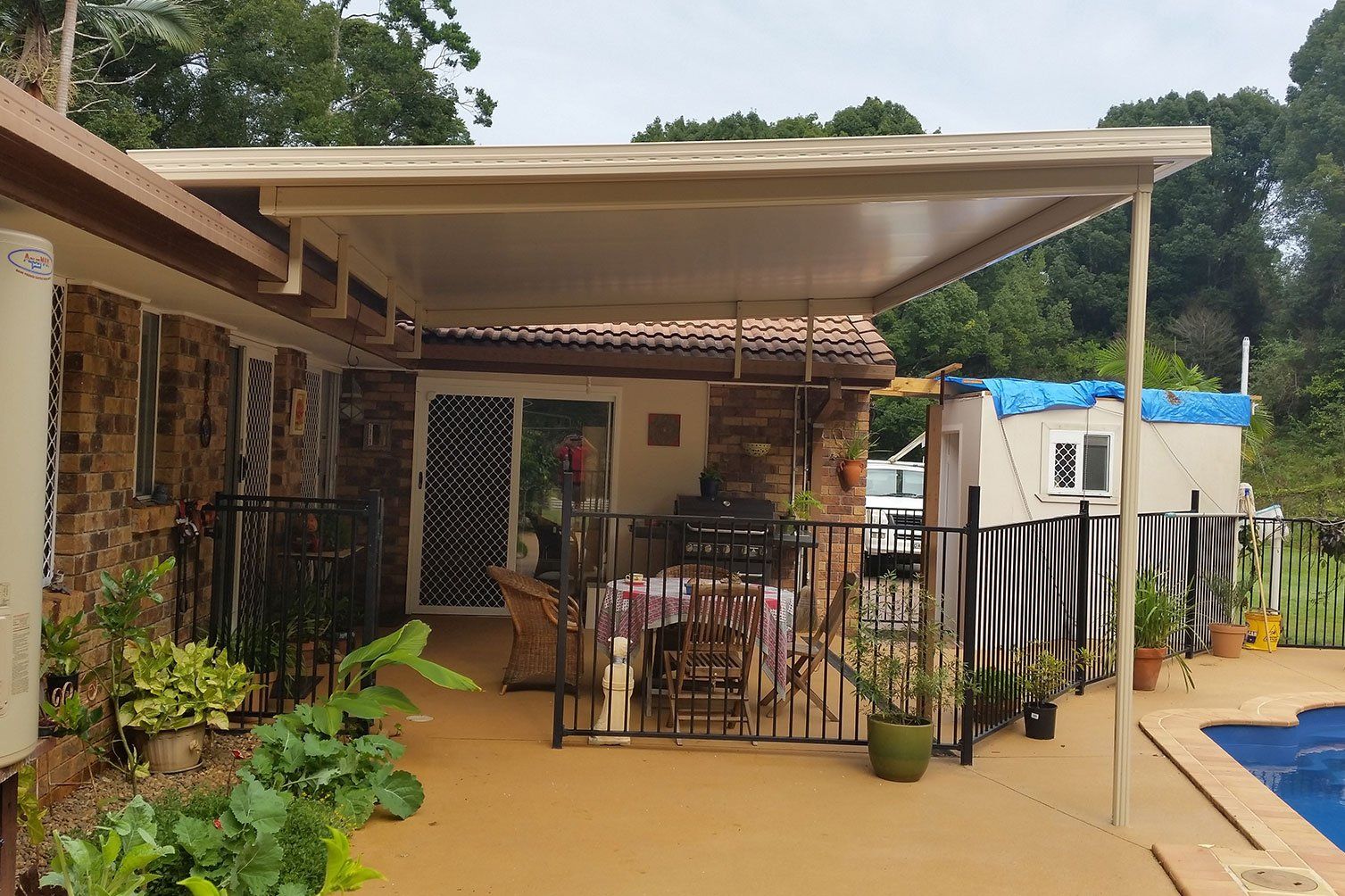 Covered patio with chairs, potted plants, and a small pool beside a house