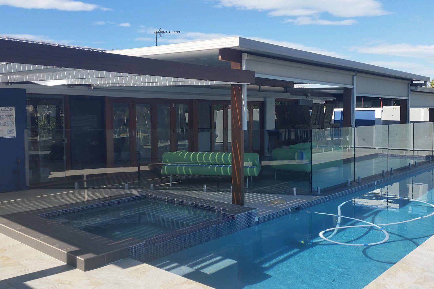 Modern house with glass railing beside a blue swimming pool under a clear sky