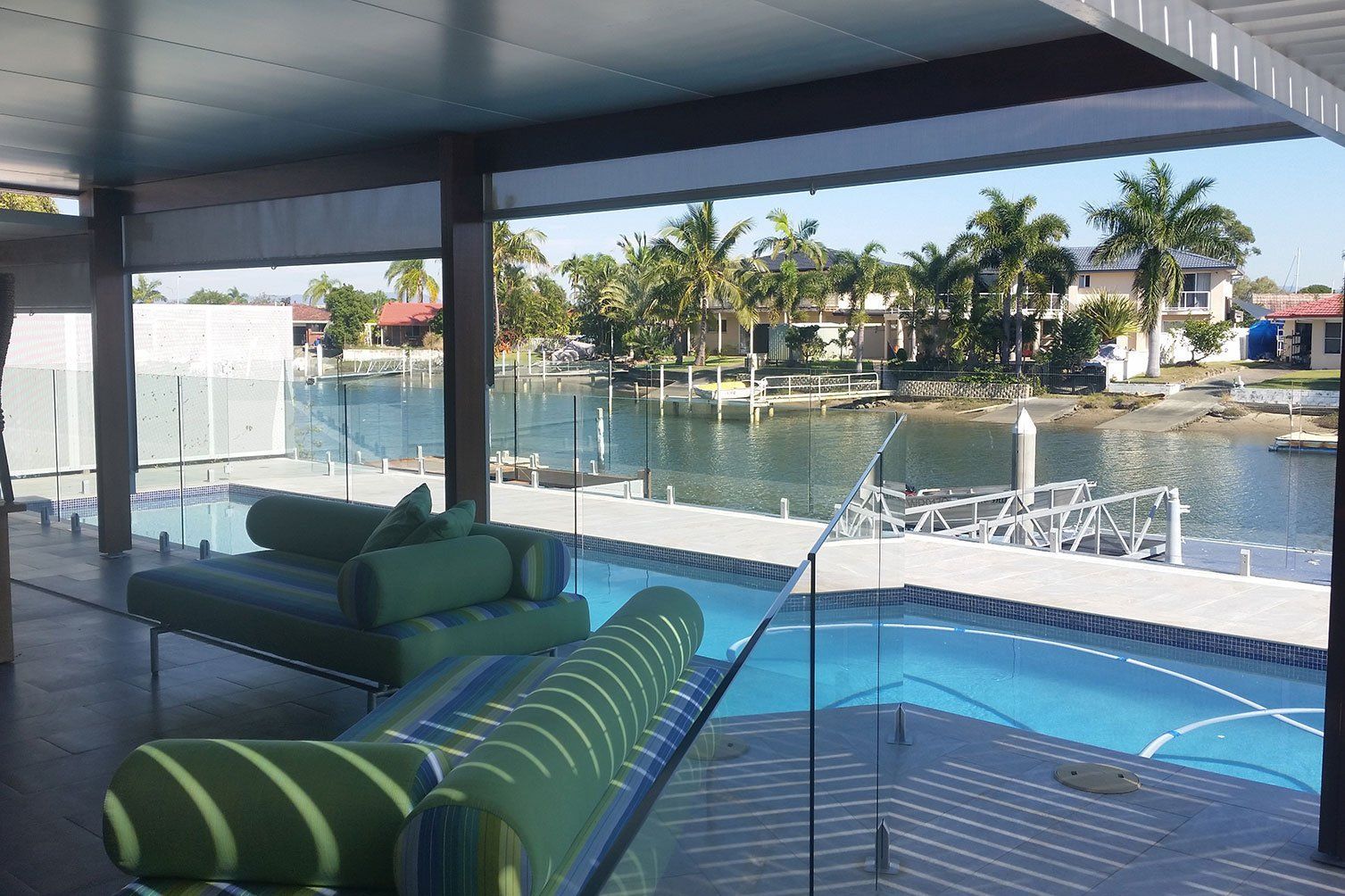 Covered waterfront patio with green lounge chairs overlooking a pool and canal at sunset