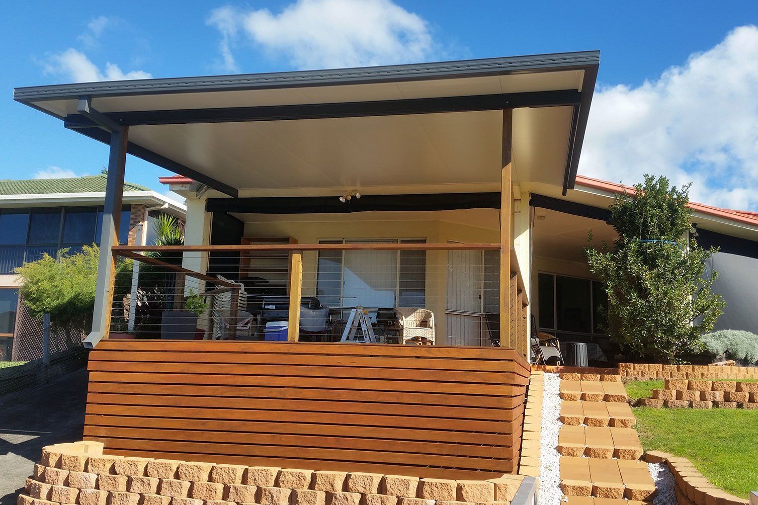 Modern house porch with a covered patio, wooden railing, and stone steps under a blue sky