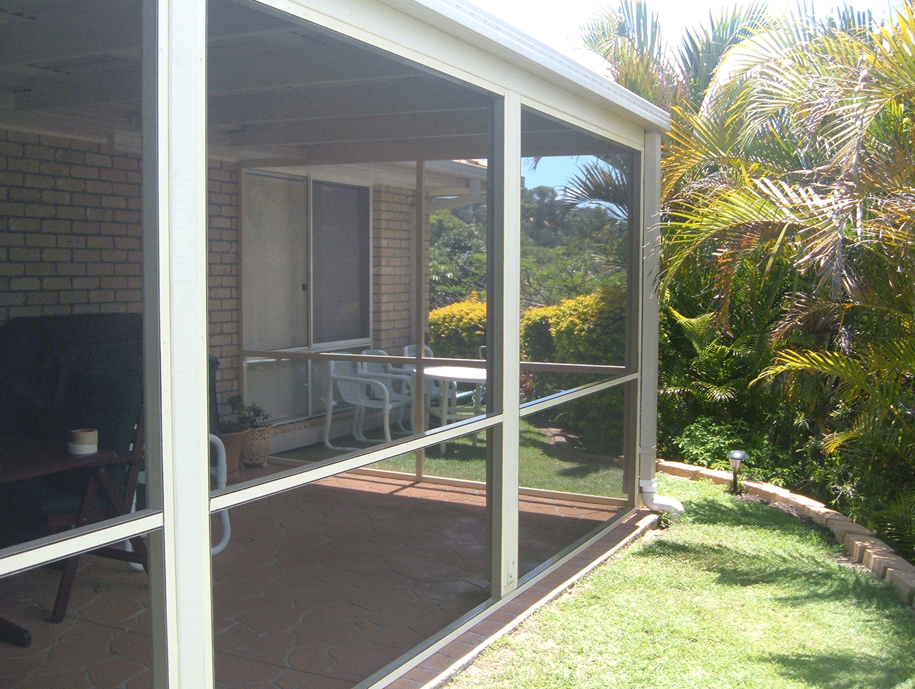 Screened patio with sliding glass doors, white chairs, and green lawn beside palm plants.