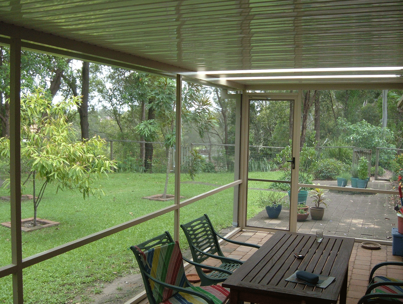 Covered patio with a wooden table and chairs overlooking a green garden.