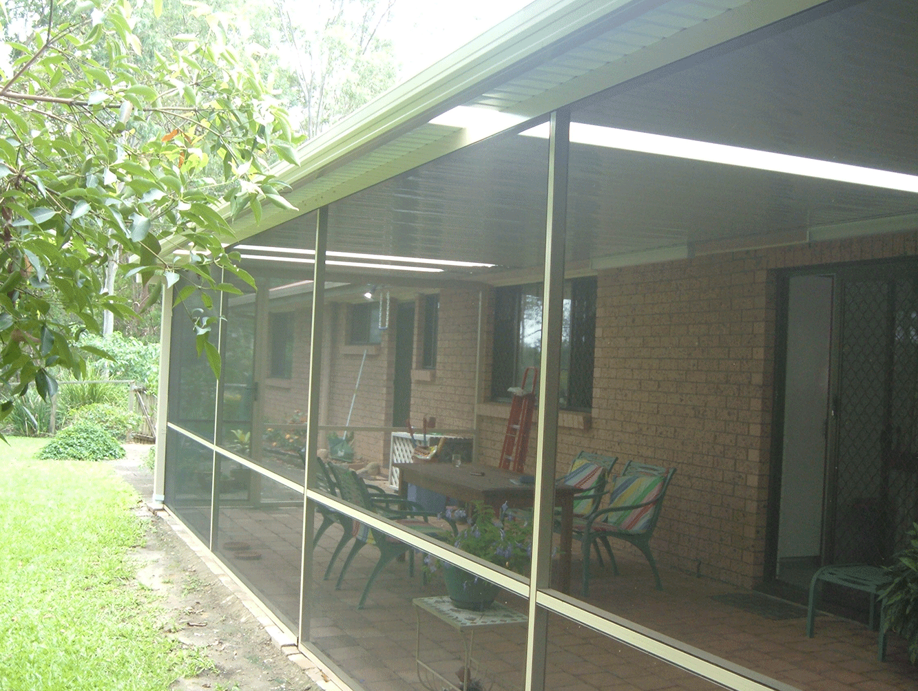 Covered brick porch with screened-in patio furniture beside a grassy yard