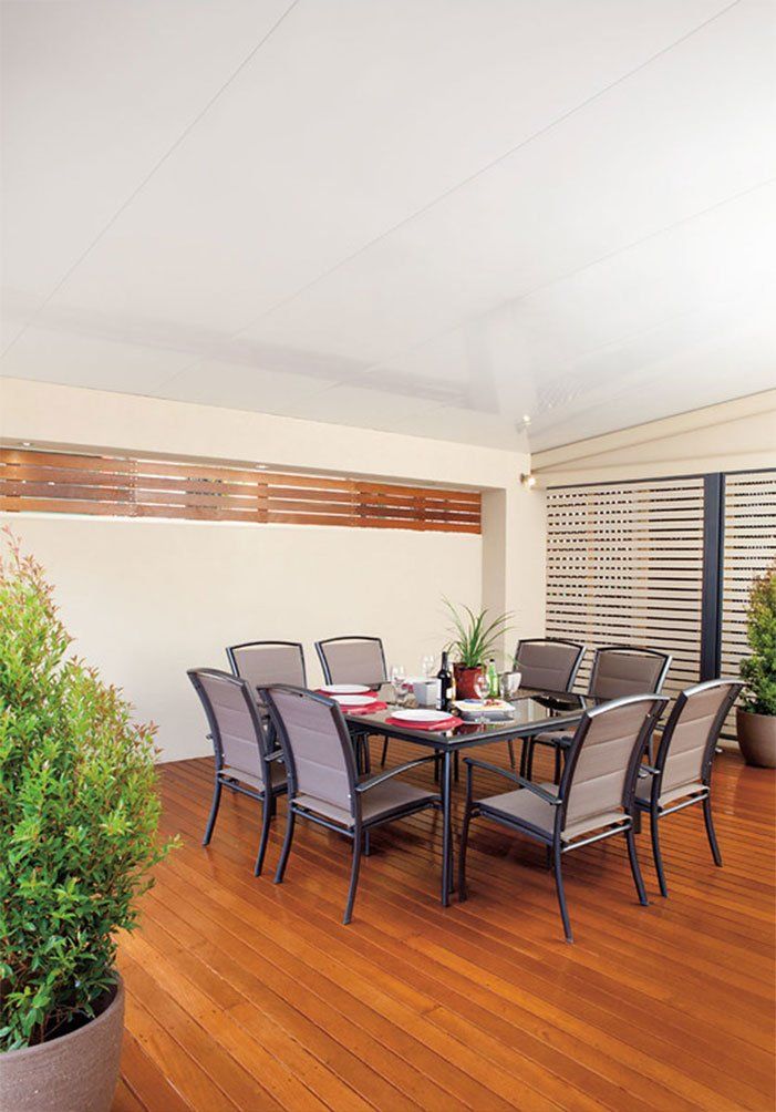 Covered patio with a dining table, chairs, potted plants, and wooden floorboards
