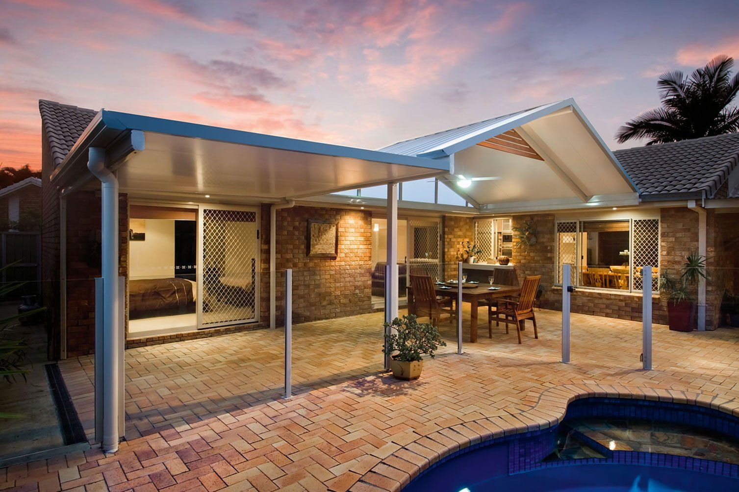 Brick patio with covered outdoor seating area and pool at dusk