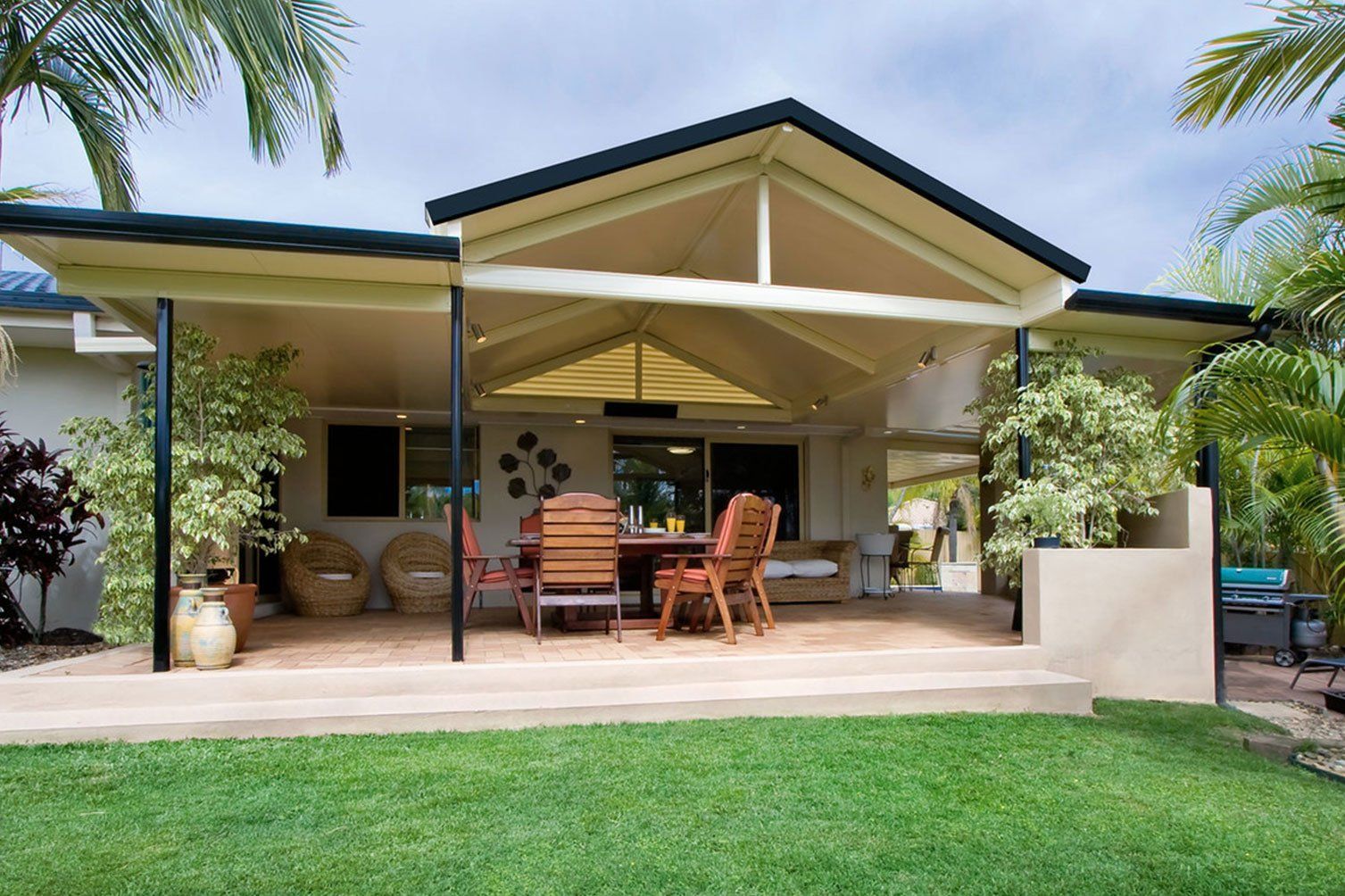 Covered patio with wicker seating, cream exterior, and lush green lawn in front of a house