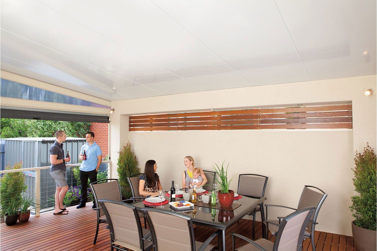 Covered patio with dining table, chairs, potted plants, and two people talking near the open doorway.