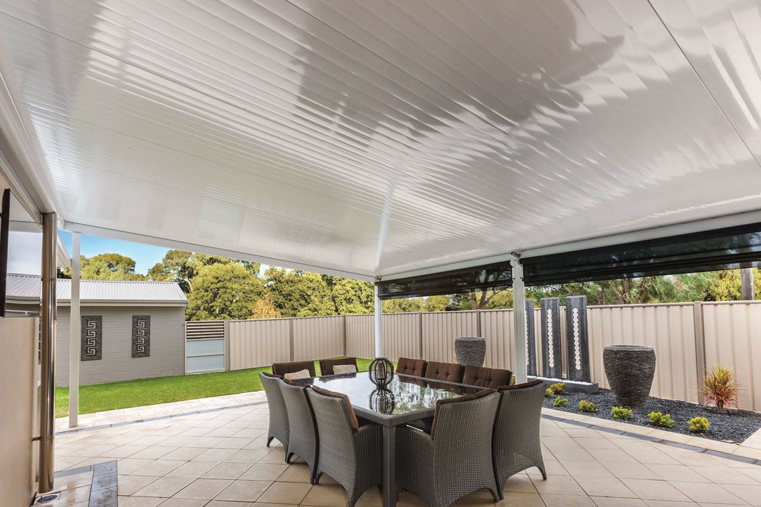 Covered patio with wicker dining set, potted plants, and a backyard lawn behind a privacy fence.