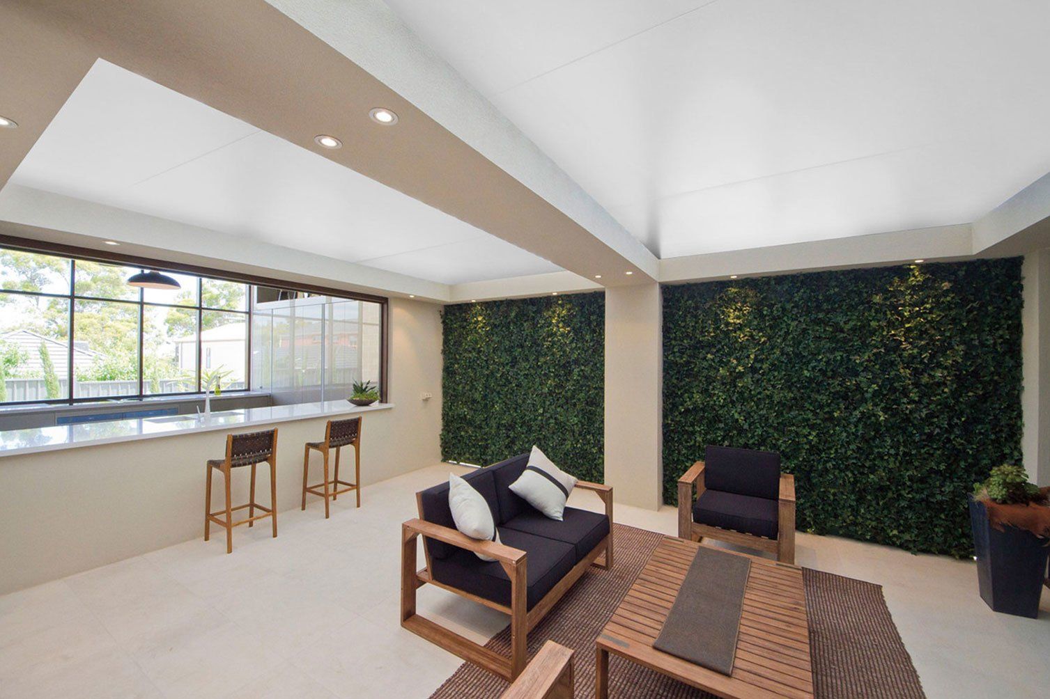 Modern living room with skylight, large windows, ivy wall panels, sofa, coffee table, stools, and potted plants