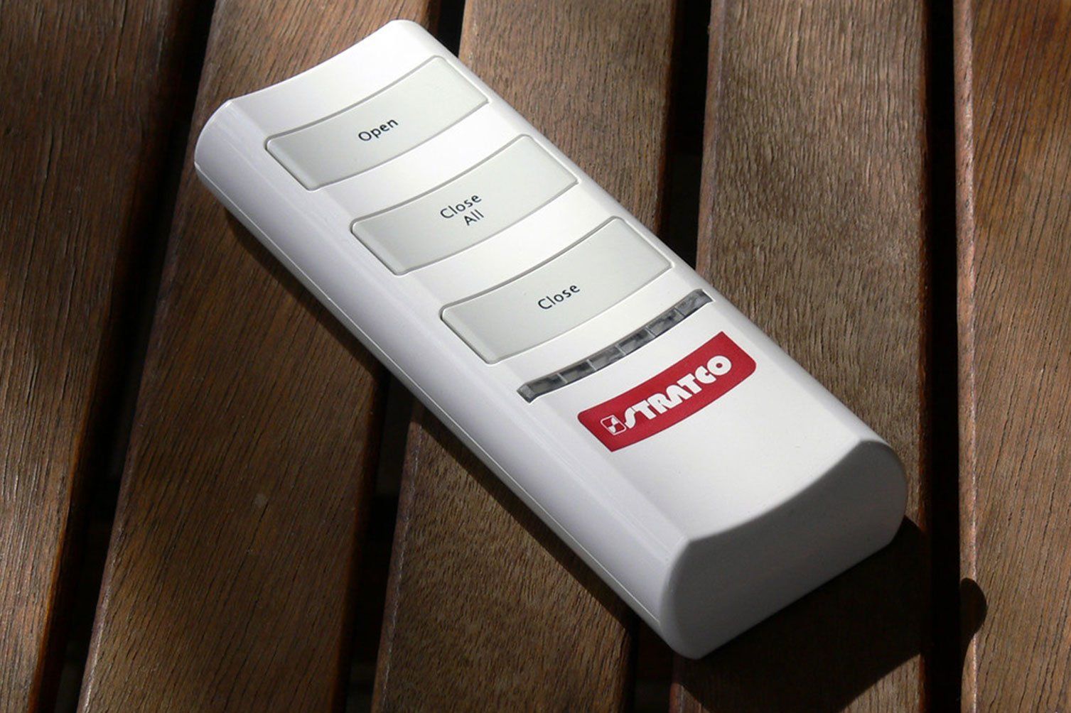 White remote control with red logo resting on a wooden slatted surface.