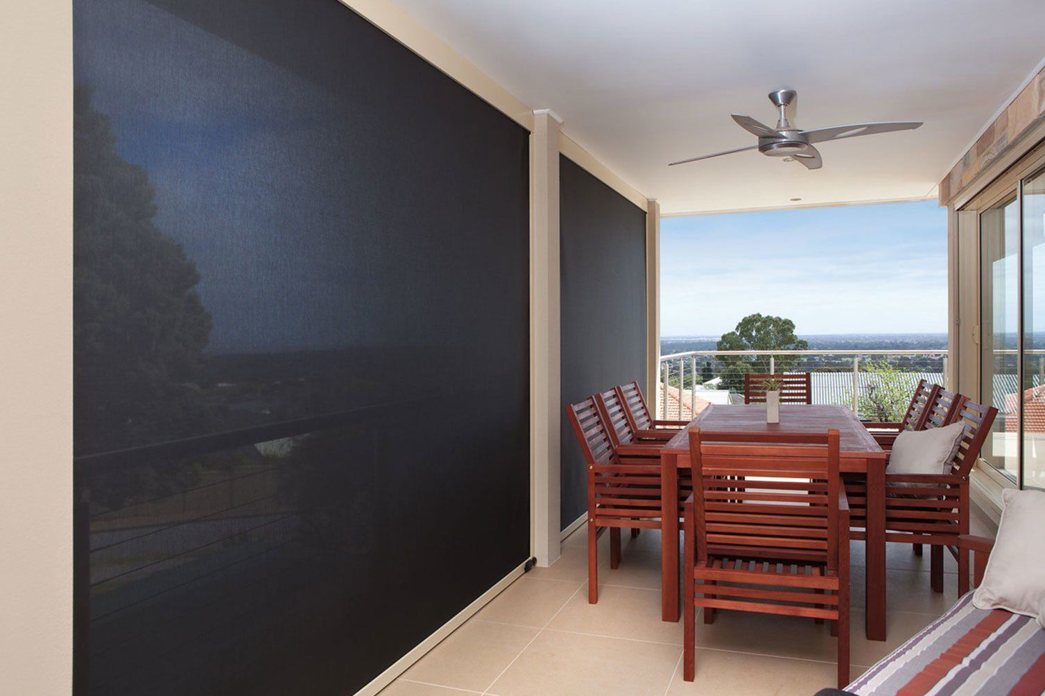 Covered balcony with red dining table and chairs, ceiling fan, and ocean view beyond a screened opening