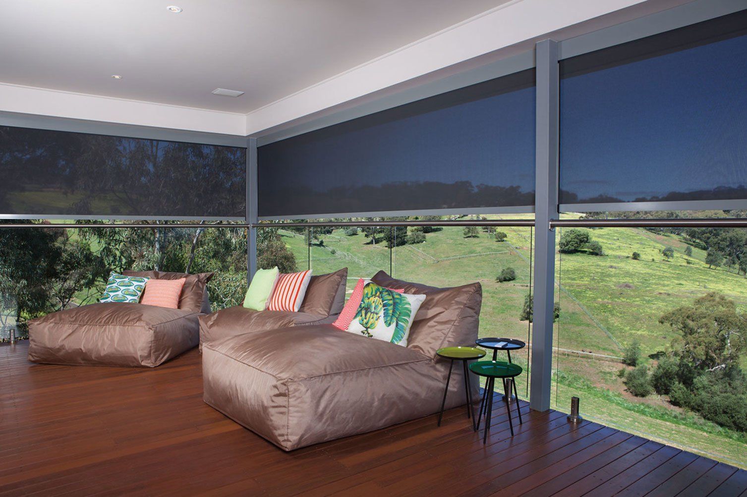 Modern lounge with brown sofa, colorful pillows, and floor-to-ceiling windows overlooking green hills