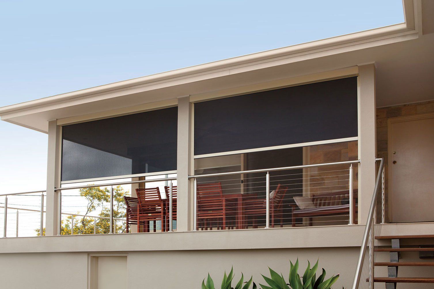 Modern house balcony with dark roller shades and patio chairs behind glass railing