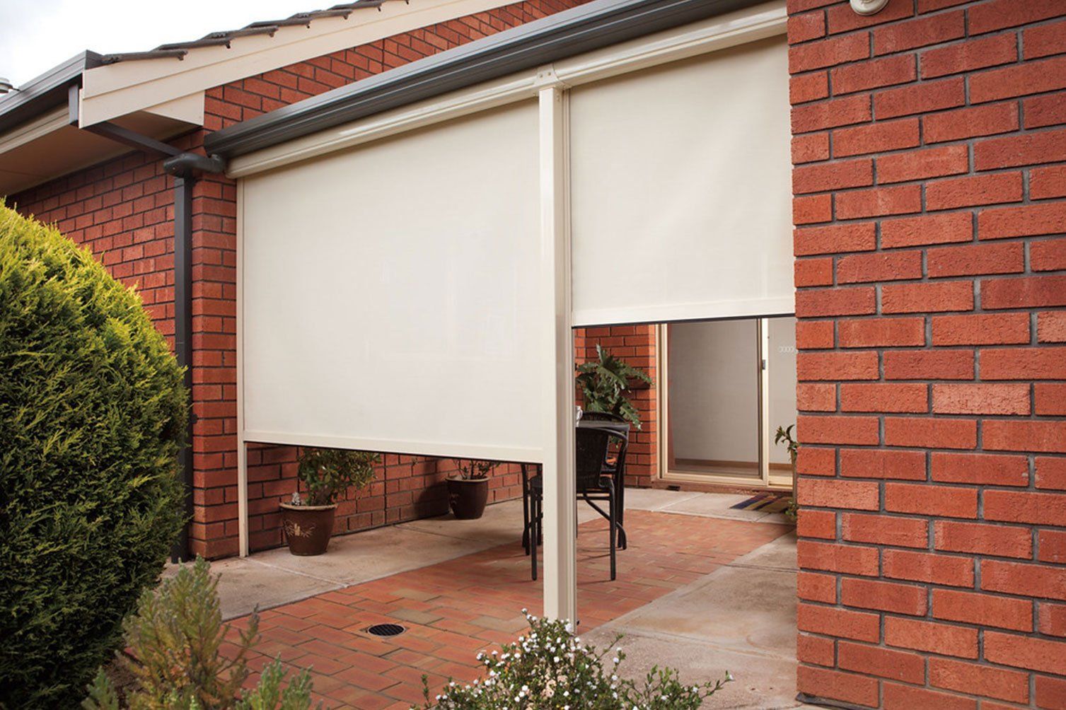 Patio with beige retractable awnings on a red brick house, covering a tiled outdoor area