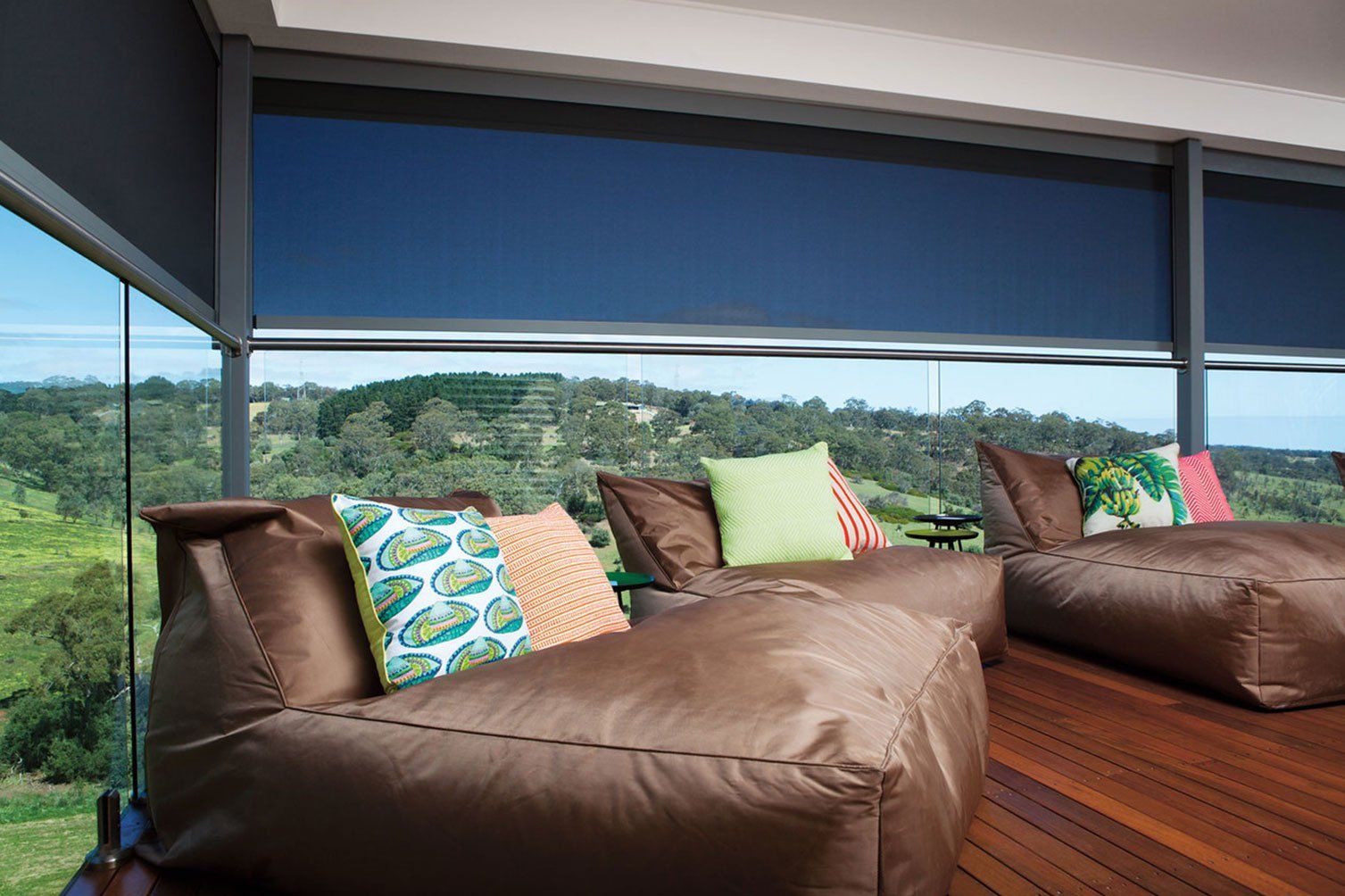 Outdoor lounge with brown beanbag sofas and colorful cushions overlooking a green landscape