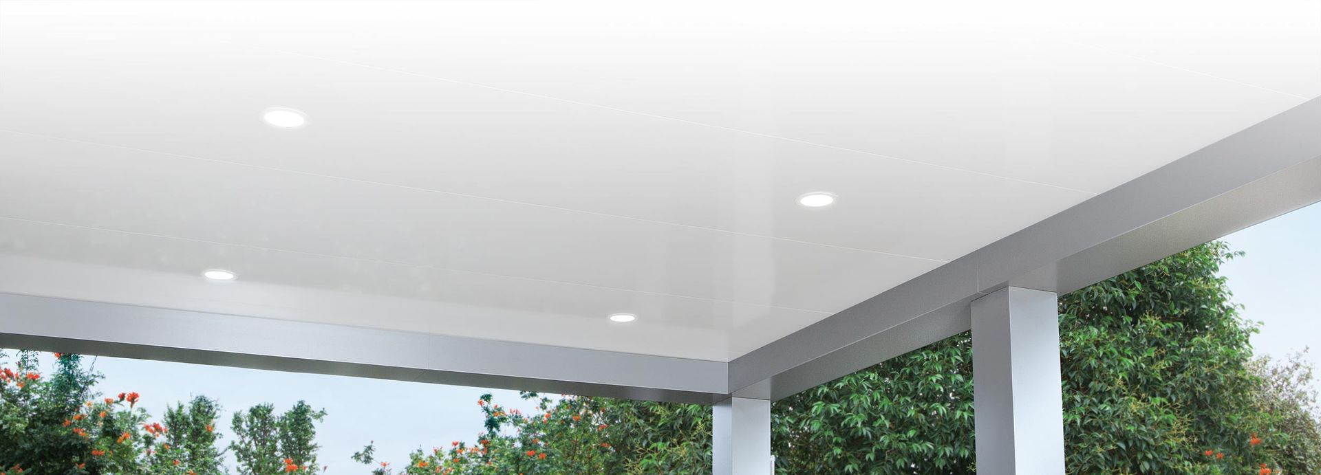 Covered outdoor patio with white ceiling, recessed lights, and open views of green trees and sky