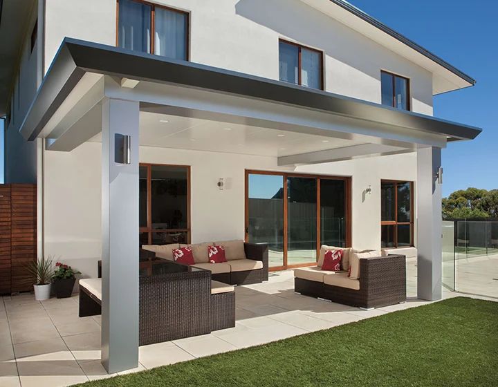 Modern white house patio with wicker seating, large glass doors, and a green lawn under a covered deck