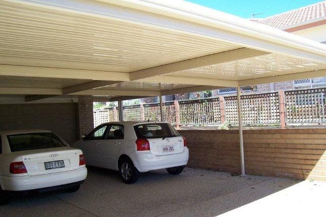Covered carport with two parked cars, one white and one silver, beside a brick wall.