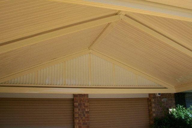 Tan carport roof with exposed beams above brick columns and brown garage doors