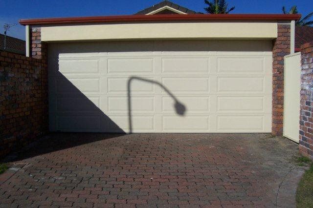 Double garage with closed cream doors and a shadow of a streetlight on the driveway.