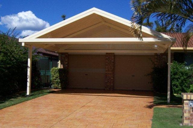 Single-story house with a wide two-car carport and brick driveway under a sunny sky