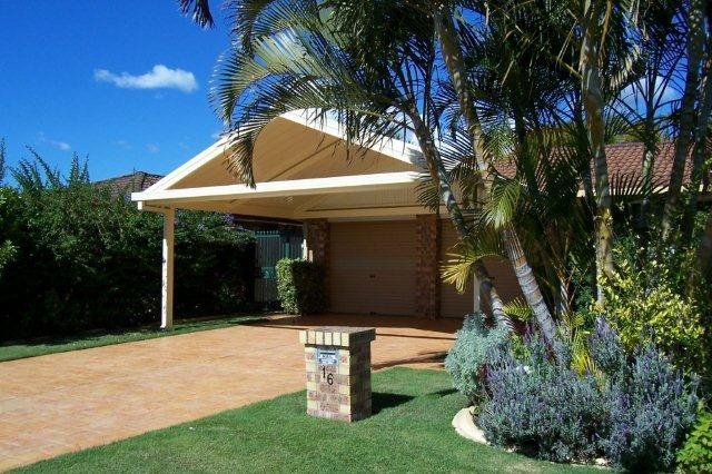 Suburban house with a carport, driveway, lawn, and palm trees under a bright blue sky