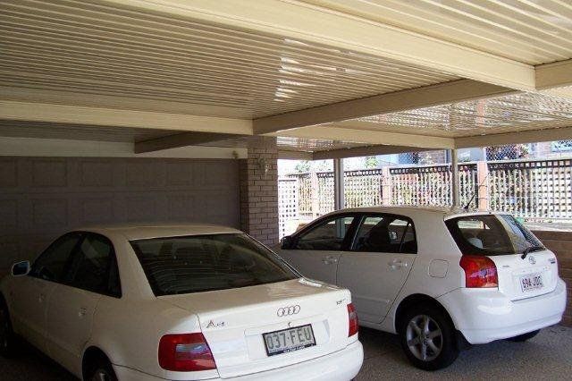Two white cars parked in a covered garage with brick pillars and a low ceiling