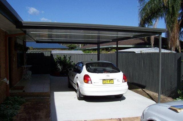 White sedan parked in a driveway under a carport beside a house and fence