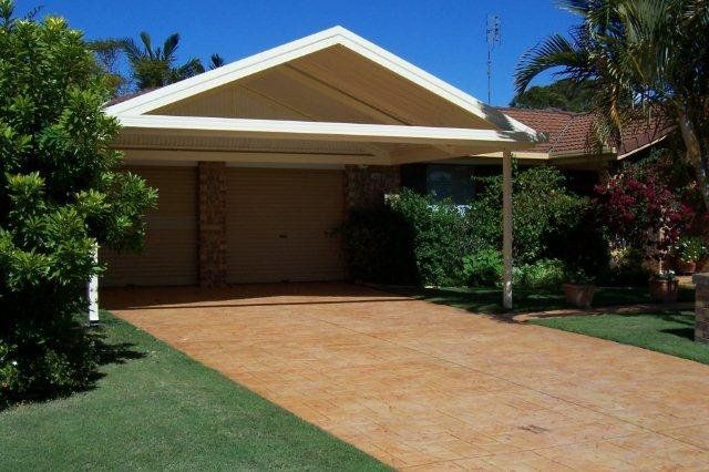 Suburban house with a tan driveway, front carport, and green lawn under a clear blue sky