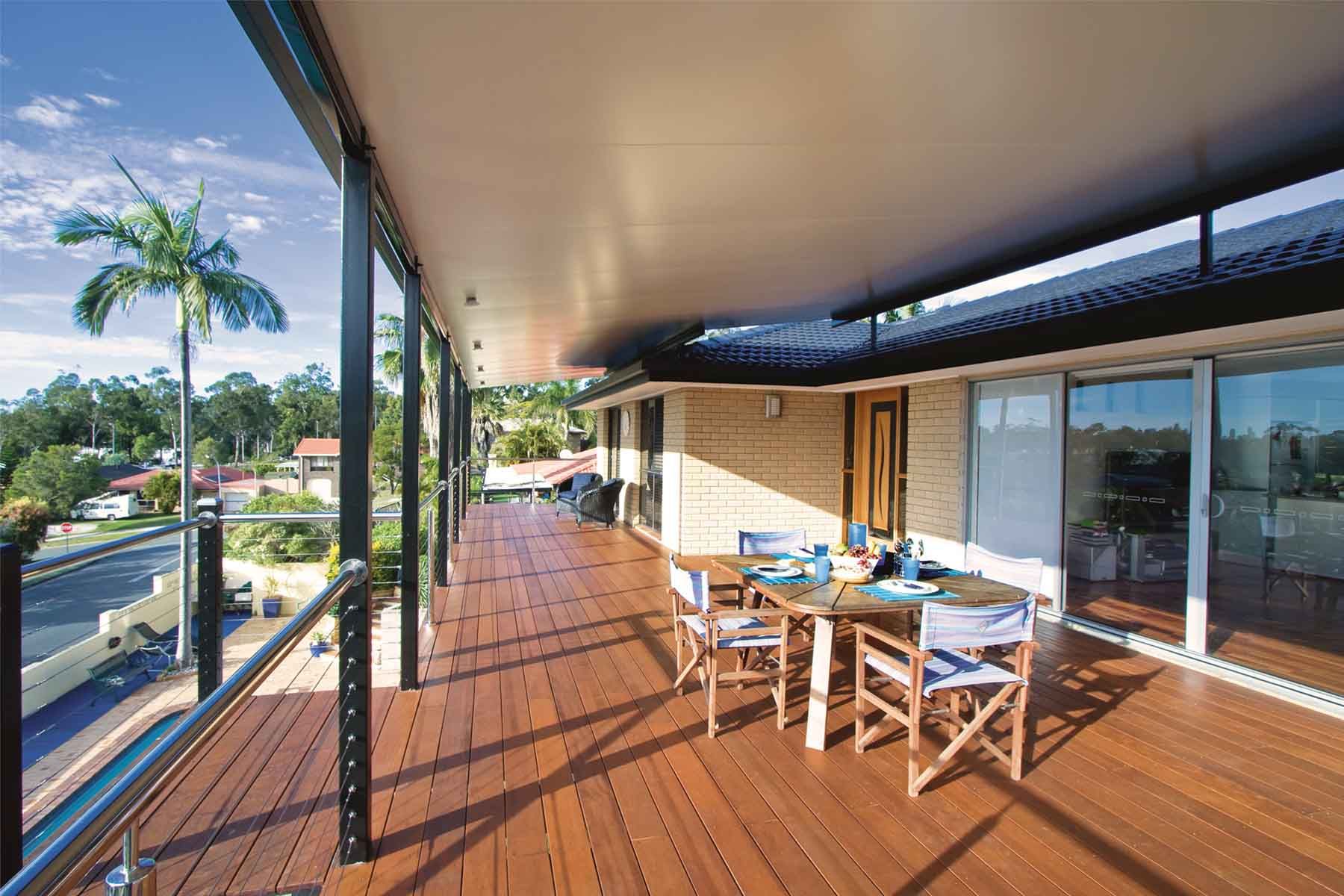 Wooden deck patio with dining table, chairs, and ocean-view glass railing in bright sunlight