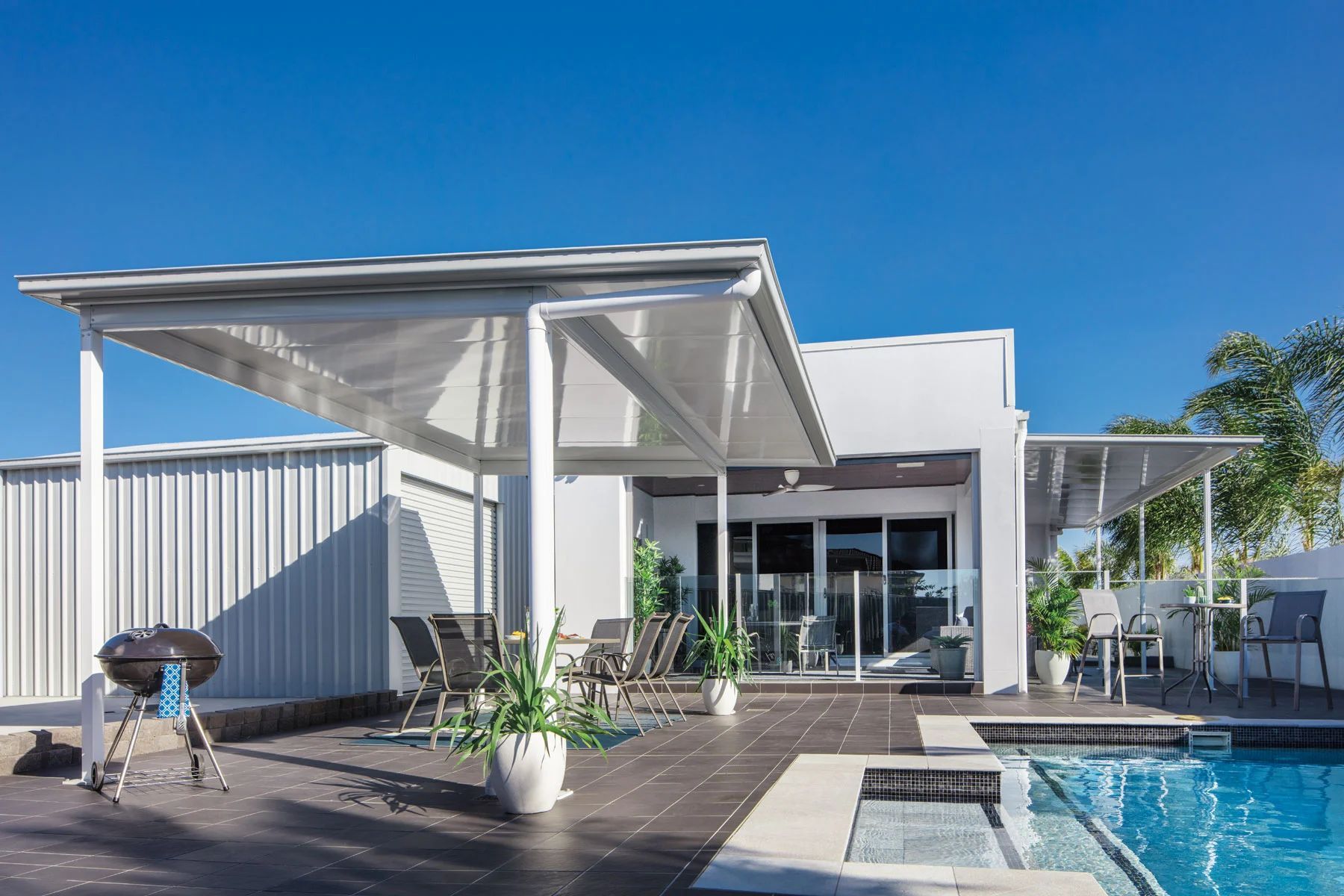 Modern patio with white pergola, lounge chairs, and a blue swimming pool under a clear sky