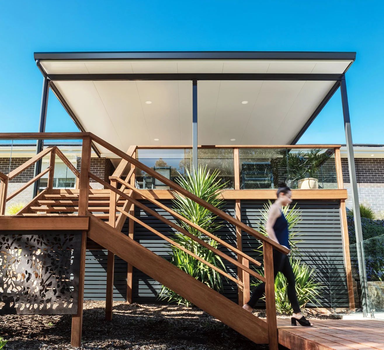 Modern house with wooden stairs and a person walking outside under a bright blue sky