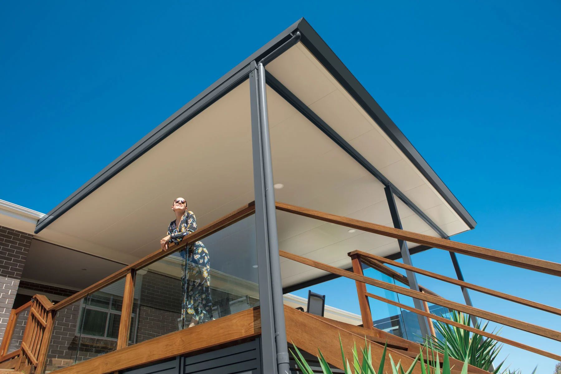 Modern house with a steep roof, wooden deck railing, and a person standing on the balcony under a blue sky