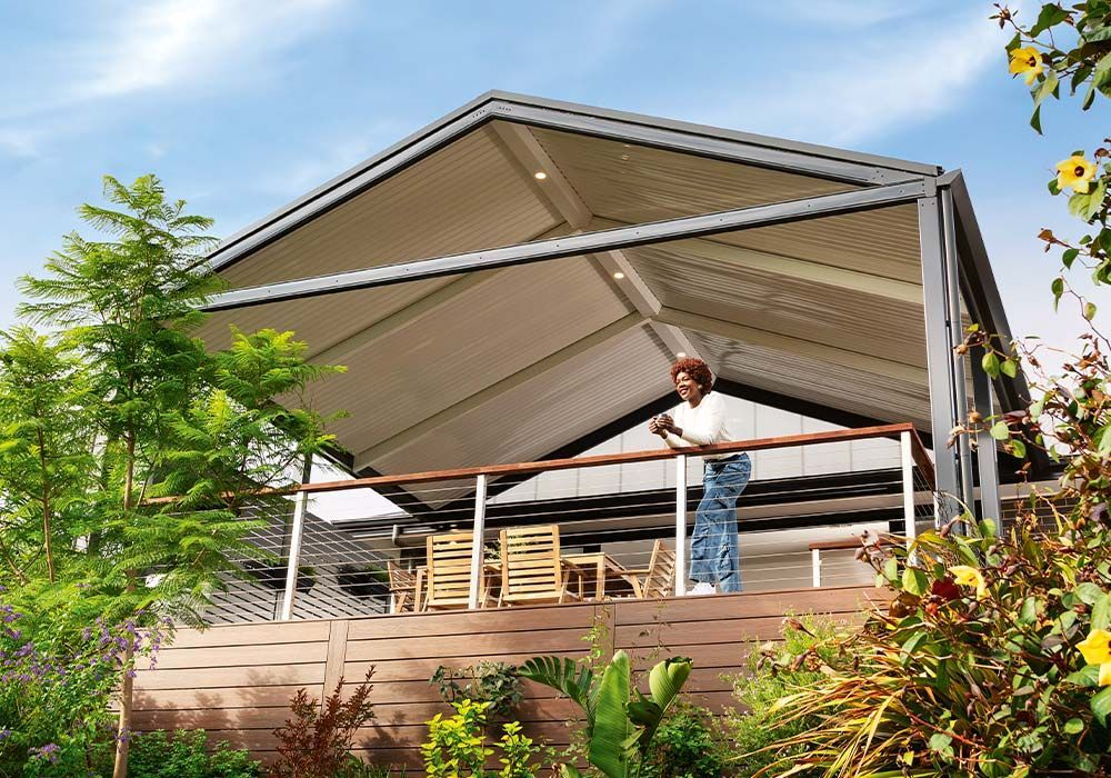 Covered patio with a person leaning on a railing, surrounded by greenery under a bright sky