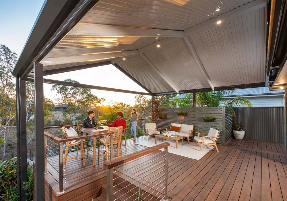 Covered outdoor deck with people seated at a table at sunset, surrounded by wood furniture and lounge chairs