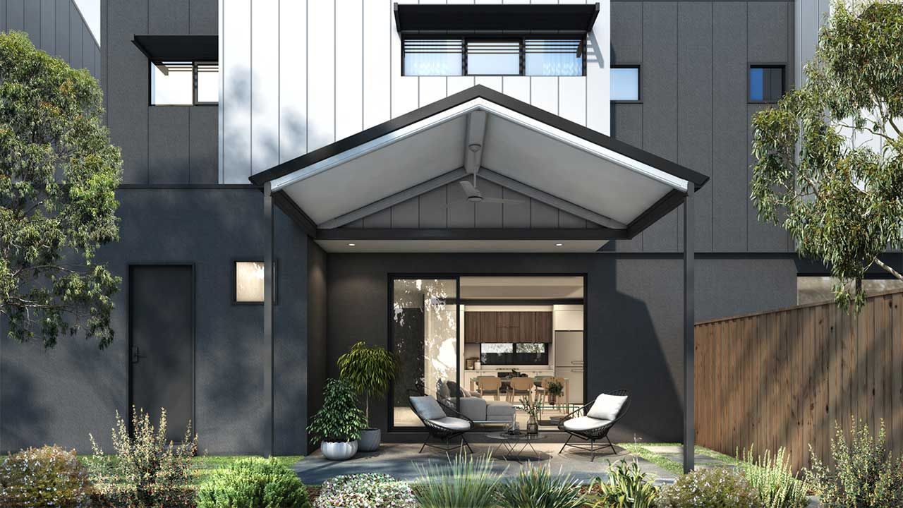 Modern patio with patio furniture under a gray awning, in front of a dark house and wooden fence.