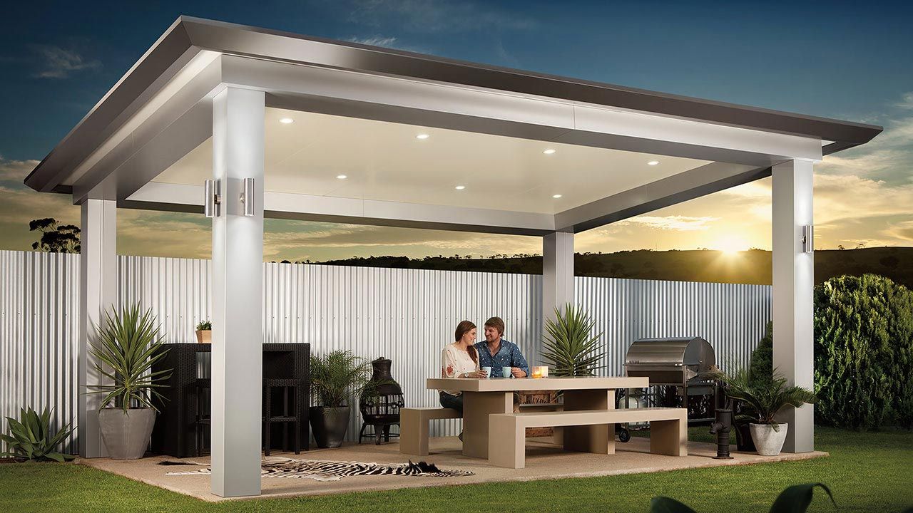 Modern patio with a covered outdoor lounge, dining table, and warm evening lighting in a landscaped yard