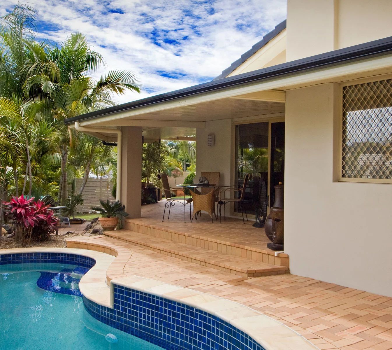 Backyard pool beside a covered patio with outdoor seating and tropical plants