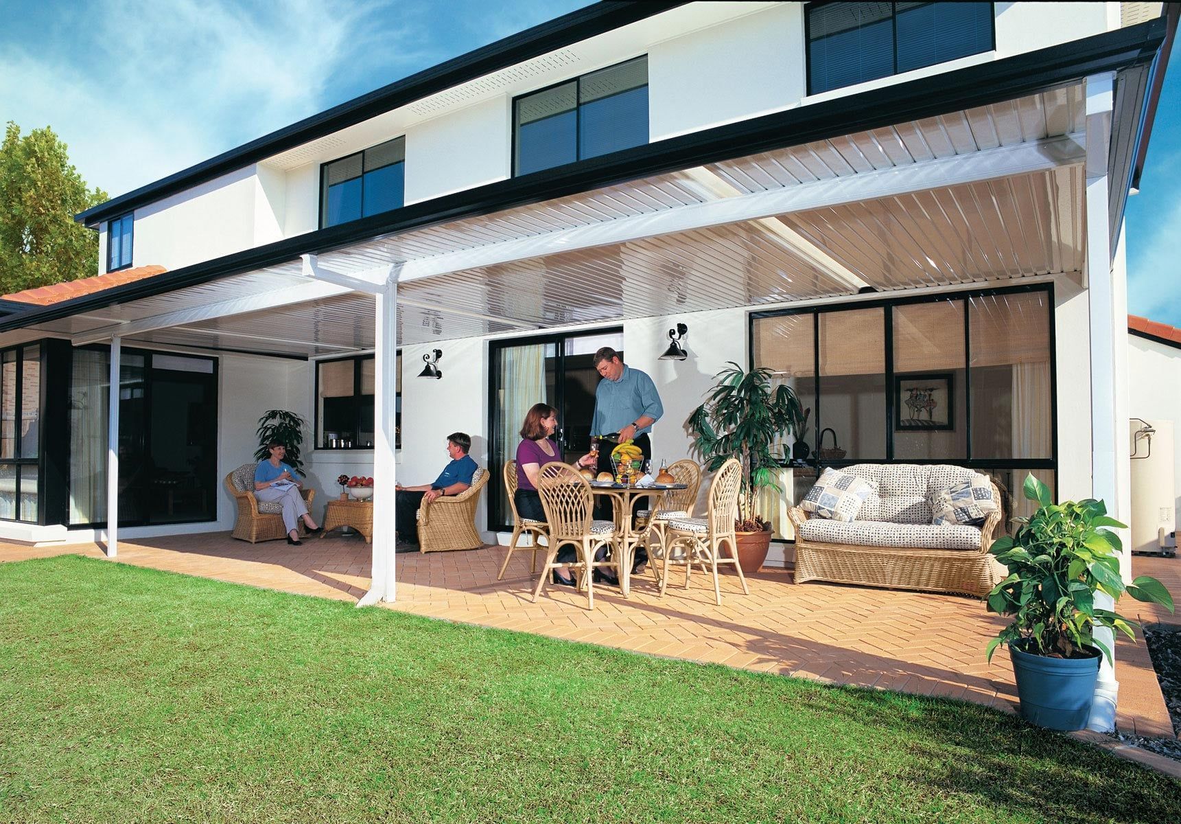 Modern house patio with people relaxing under a covered veranda, lawn in front, and outdoor seating