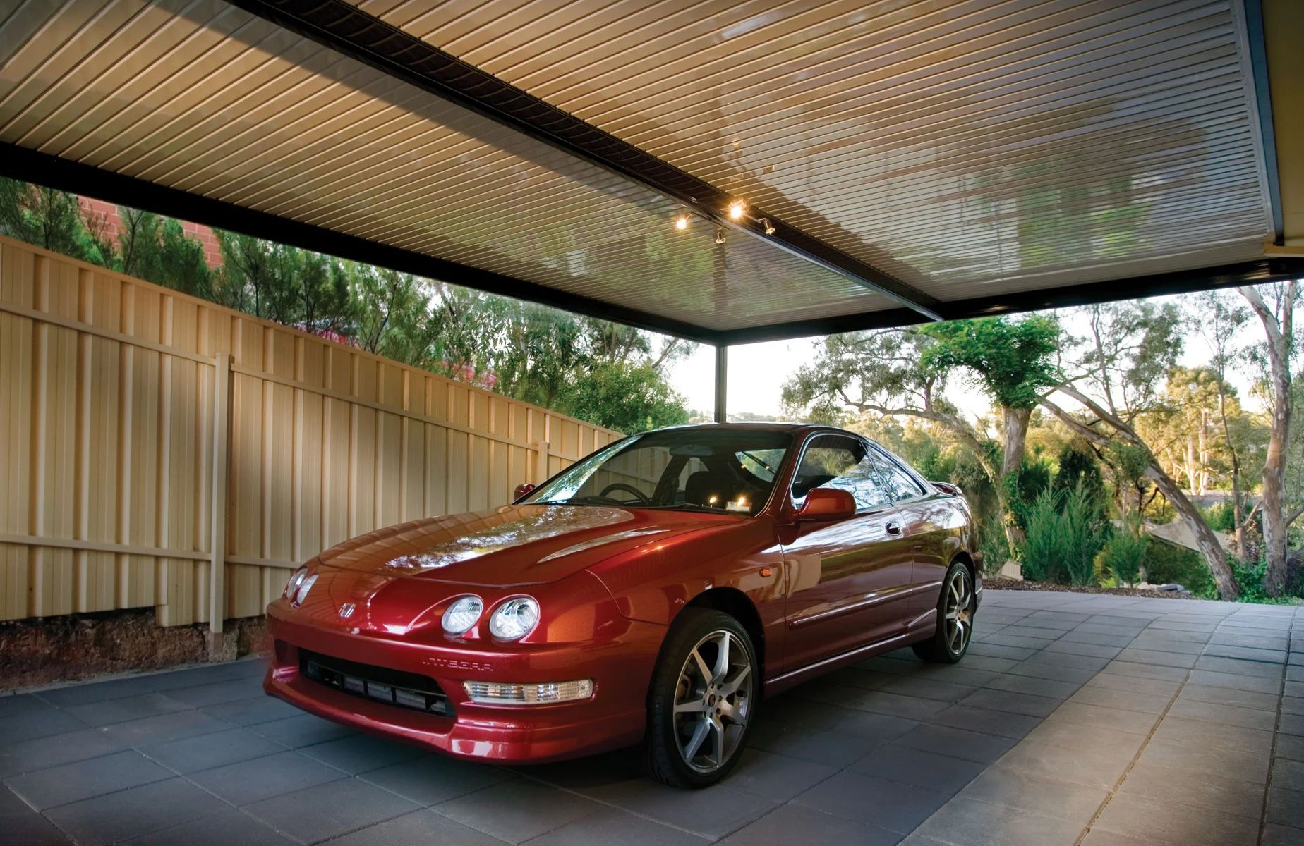 Red sports car parked under a covered patio with tiled floor and garden views