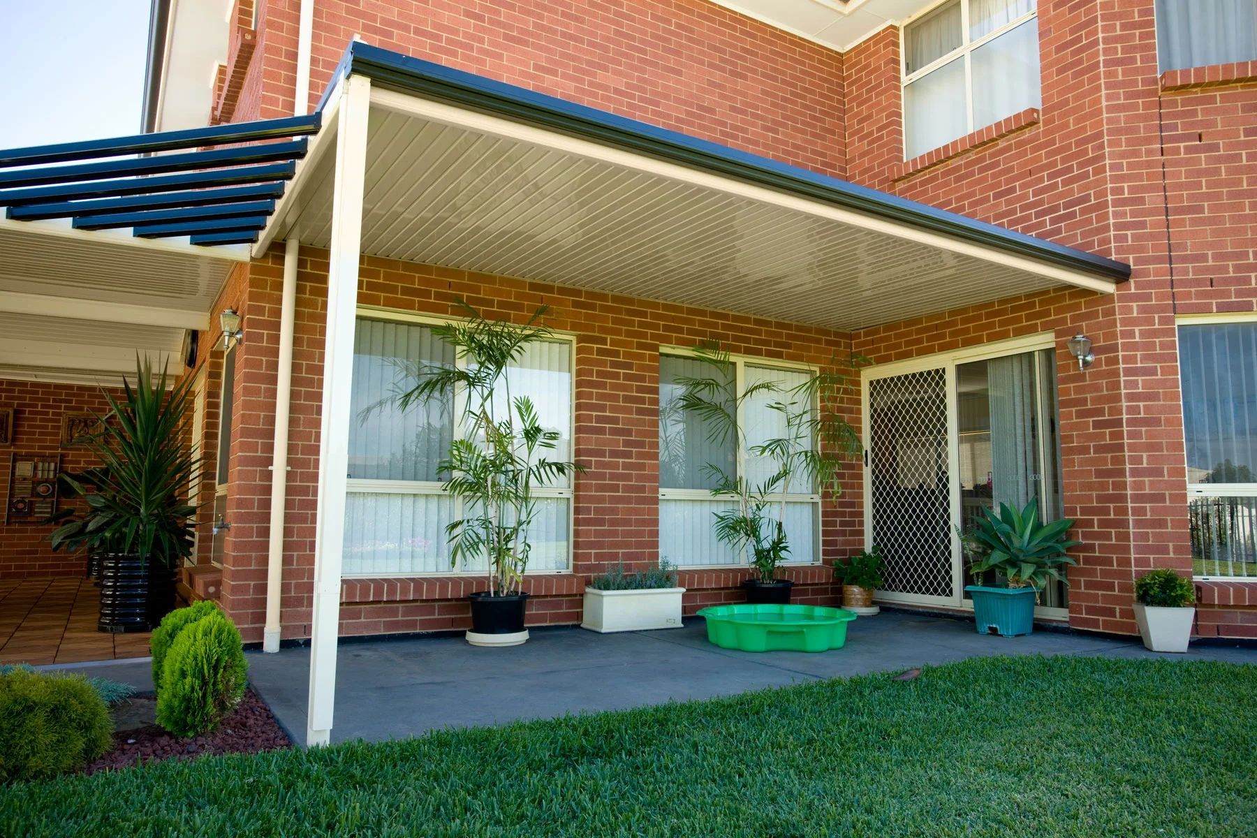 Brick house patio with covered porch, white columns, potted plants, and a green lawn