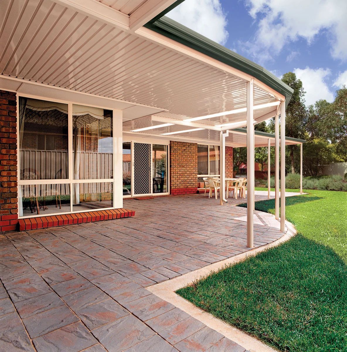Covered brick patio with white columns, sliding glass doors, and a green lawn beside a brick house.