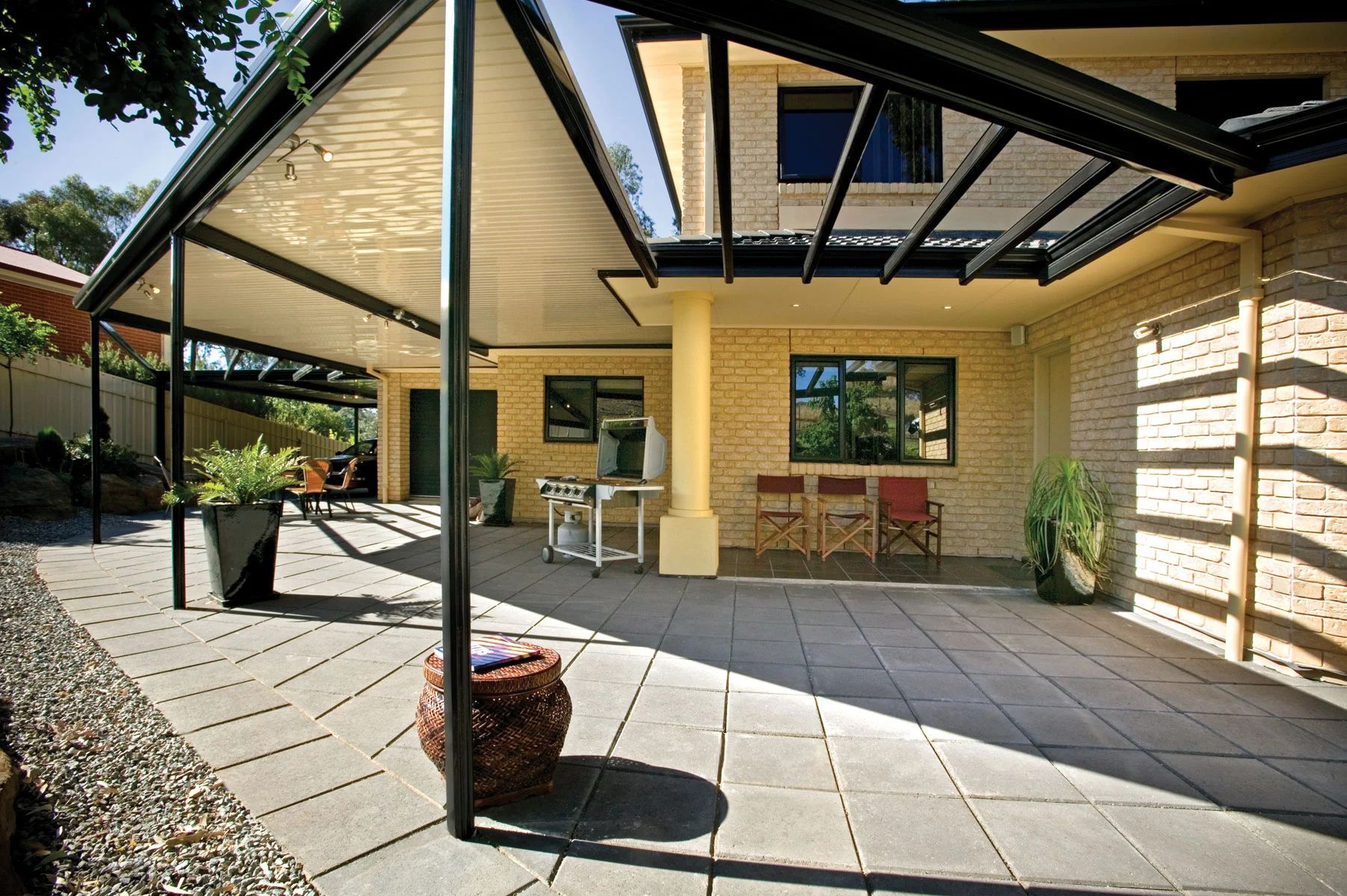 Covered patio with brick wall, black metal beams, paved floor, and outdoor seating in a sunny yard