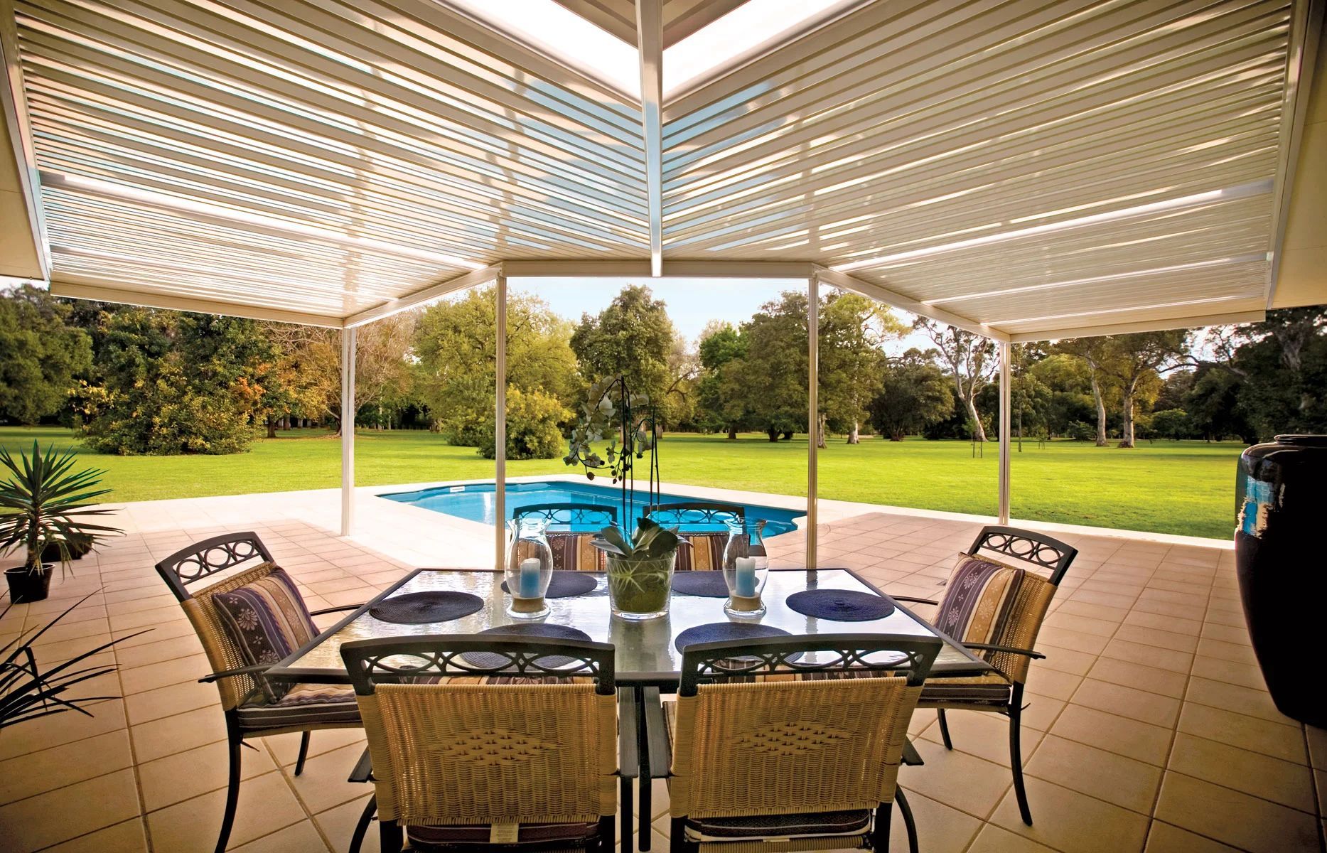Covered patio with dining table and chairs overlooking a pool and green lawn