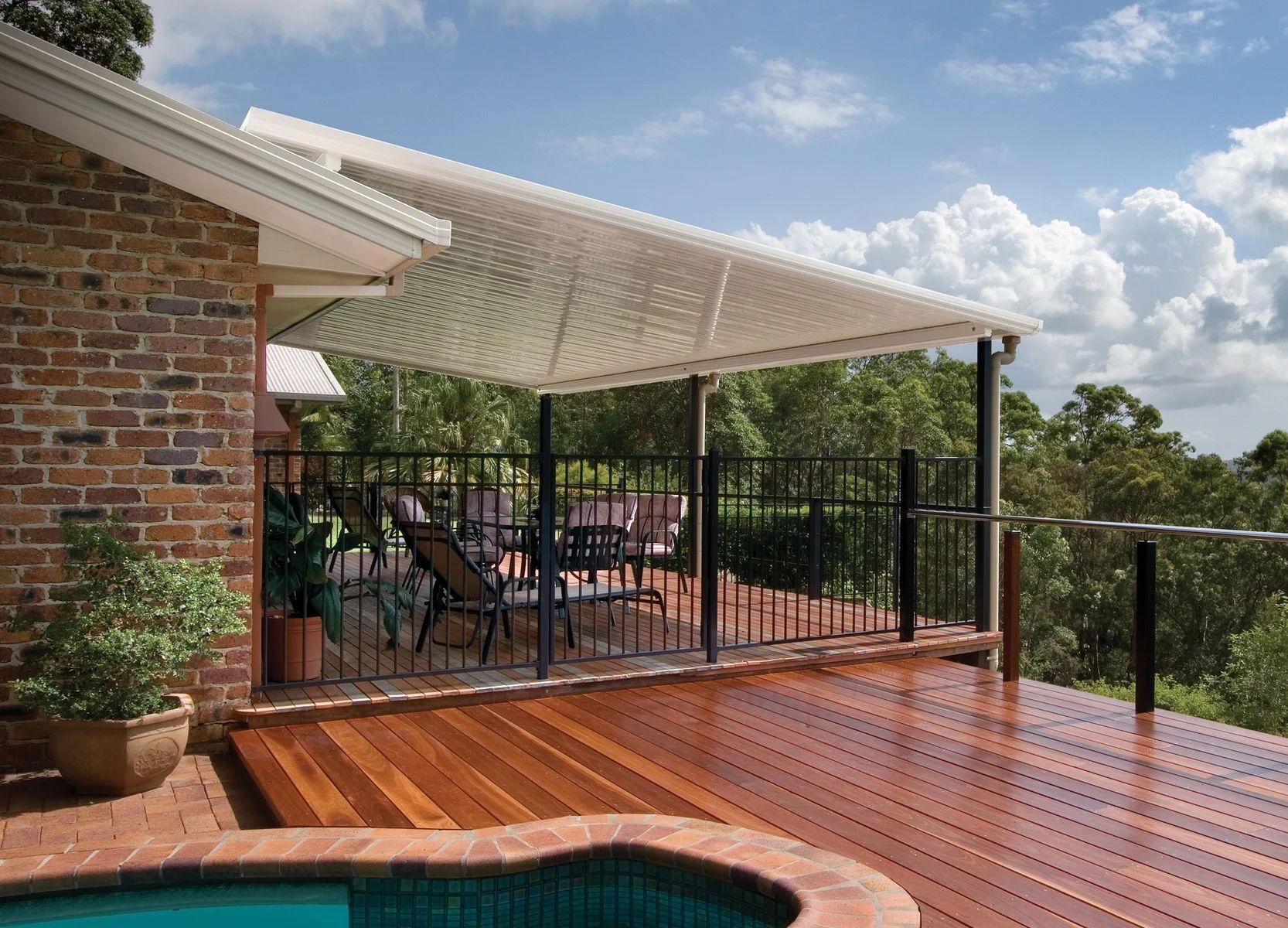 Backyard patio with wooden deck, brick house, pool, and shaded seating area