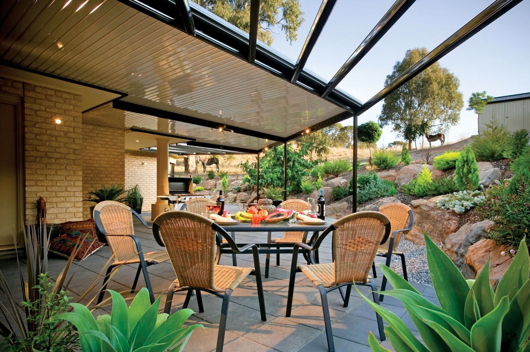 Patio dining area with wicker chairs, a table, and a black pergola in a landscaped garden