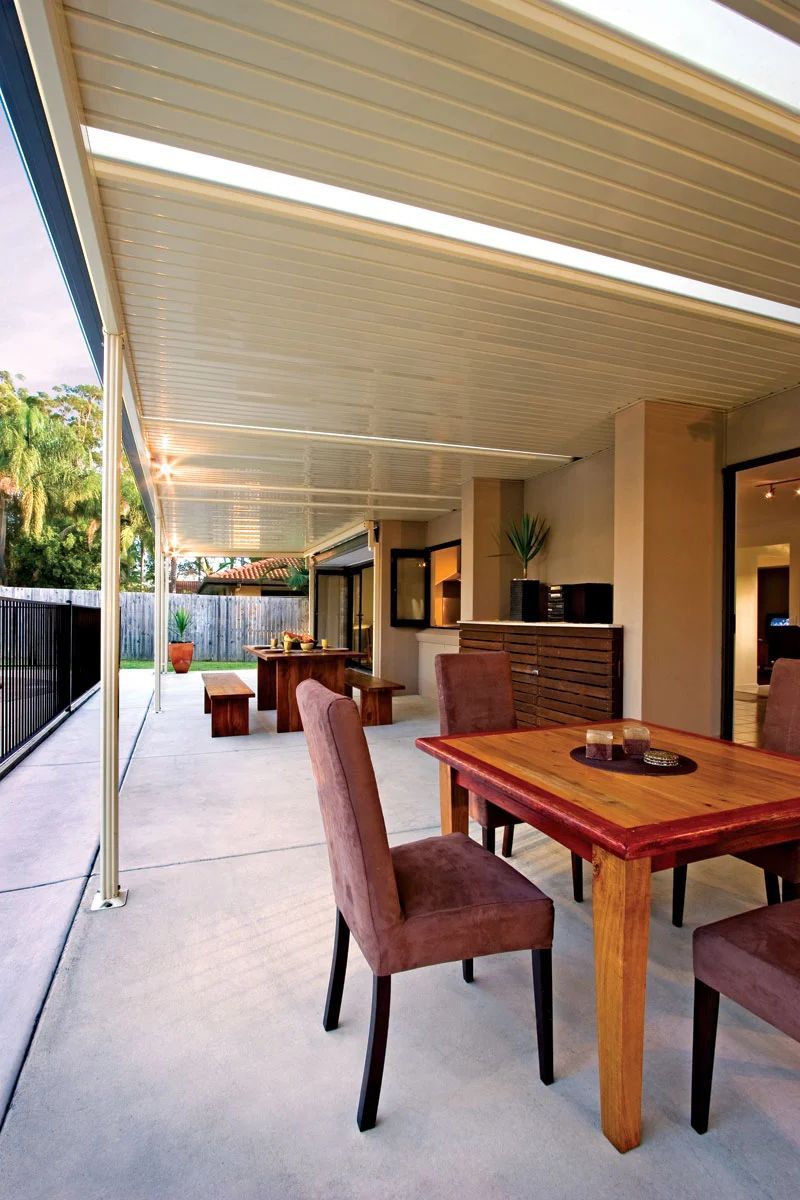 Covered outdoor patio with wooden tables and chairs, brick bar, and a view of the pool and garden.