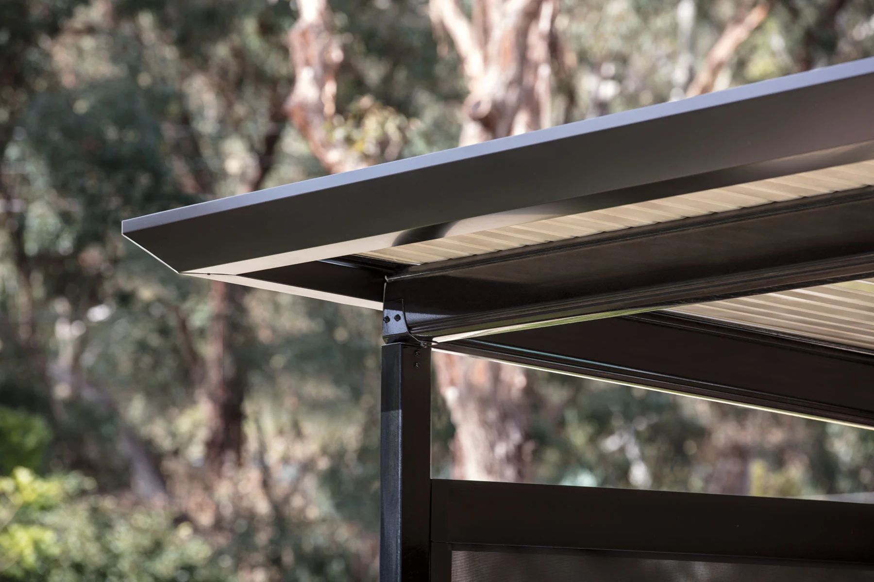 Close-up of a black metal roof edge against blurred trees outdoors