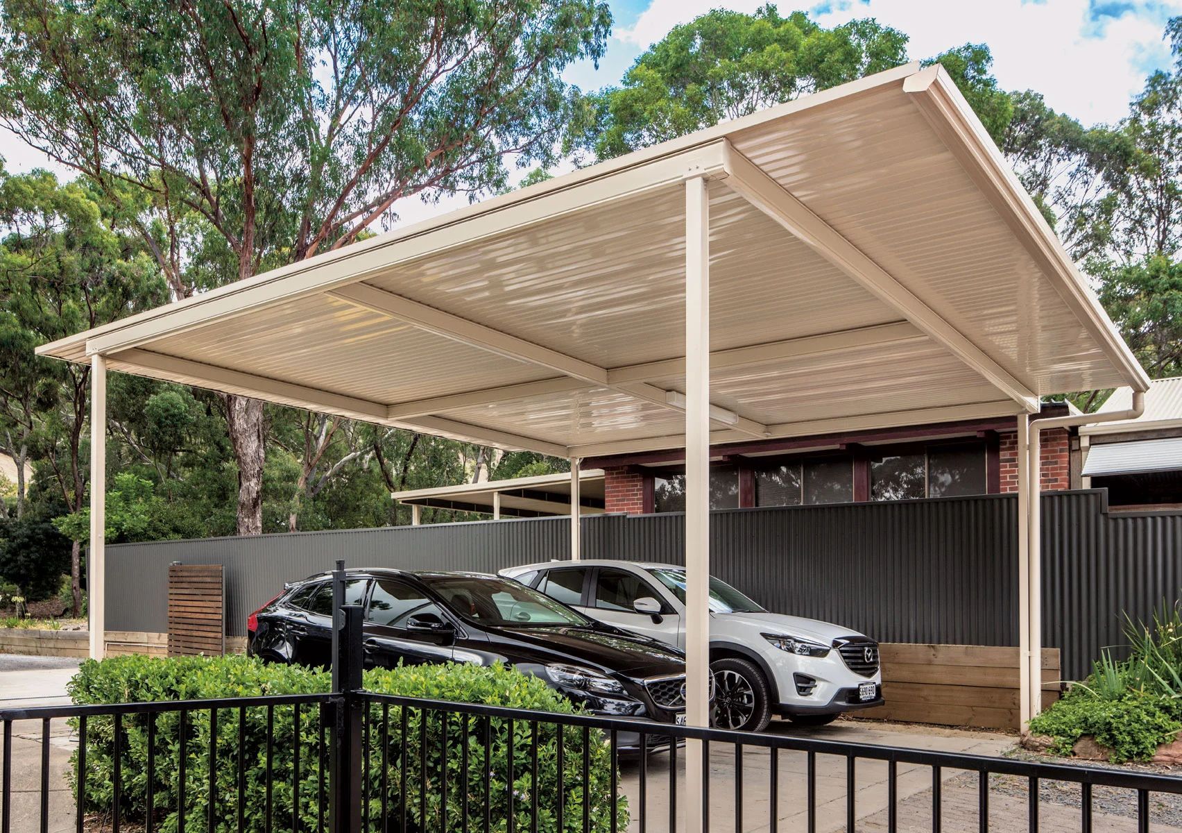 Covered carport with two parked cars beside a black fence and trees